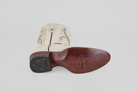 A single Austin - White - Round Toe cowboy boot lies on its side, displaying decorative stitching, a brown leather sole with AV230 embossed branding, and a textured black heel.