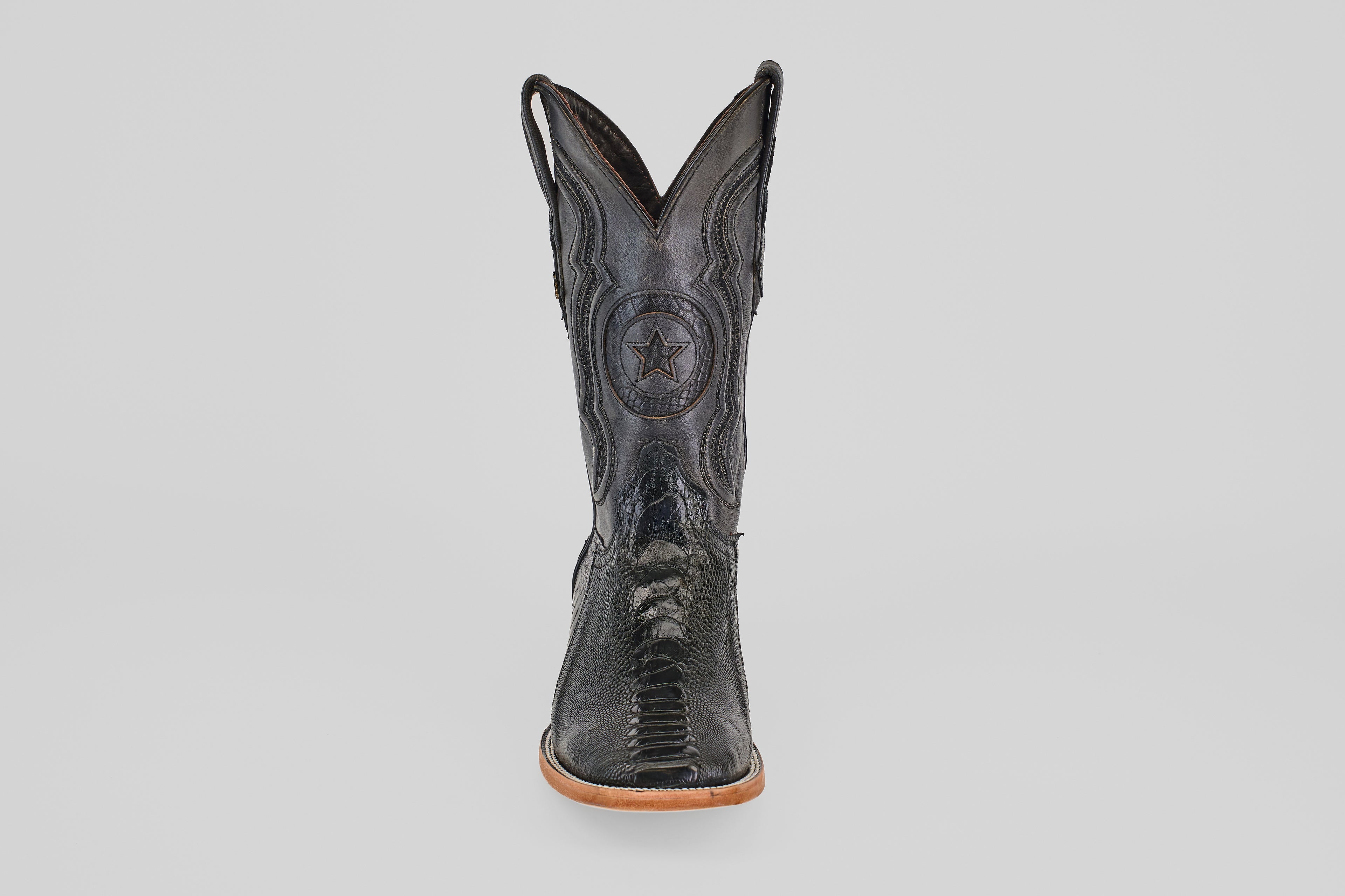 The Austin Leg - Black - Square Toe boot features decorative stitching, a star emblem on the shaft, and a light tan sole. Photographed from the front on a plain light gray background, it's ideal for square toe boot enthusiasts.