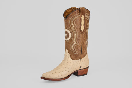 The Austin - Bone - Snip Toe showcases a single western boot with a tan shaft, decorative stitching, and a light textured ostrich leather foot, set upright on a plain light gray background. A stylish choice for ostrich leather cowboy boot lovers.