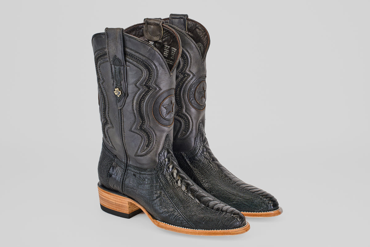 The Austin Leg - Black - Roper Toe boots feature intricate stitching, embossed star designs, decorative pull straps, and a light brown wooden heel and toe, pictured side by side on a light gray background.