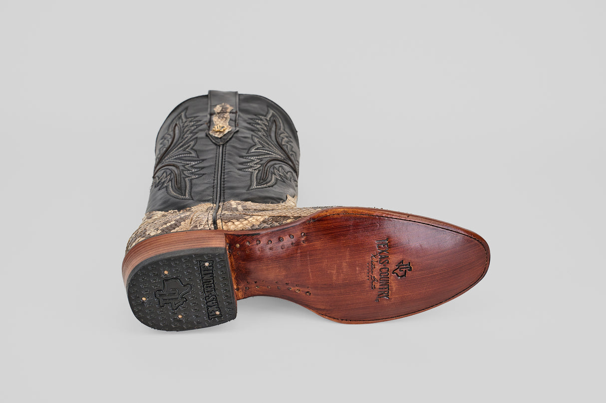 The Tanner - Natural - Roper Toe boot is displayed on its side, featuring a black embroidered shaft, brown textured foot, and a smooth natural leather sole with branding and a rubber heel cap.