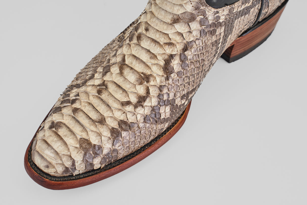 Close-up of the Tanner - Natural - Roper Toe boot’s pointed toe, crafted from natural beige and brown python leather, with a wooden sole and dark stitching detail.
