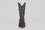 The Tanner – Matte Black – Roper Toe boot stands upright on a light brown sole, featuring a scaly texture and stitched star emblem on the shaft, showcasing western style against a clean white background.