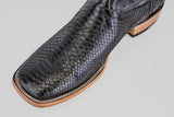 A close-up of the Tanner - Black - Square Toe cowboy boot displays black snakeskin, a square toe, detailed stitching, and a light brown leather sole set against a light gray background.
