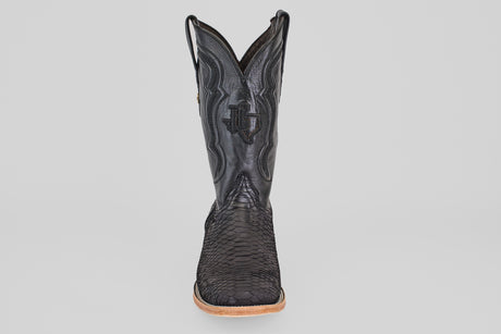 A single Tanner - Matte Black - Square Toe cowboy boot with a textured, snakeskin-inspired finish, matte black color, square toe, decorative stitching, and light brown sole is shown facing forward against a plain white background.
