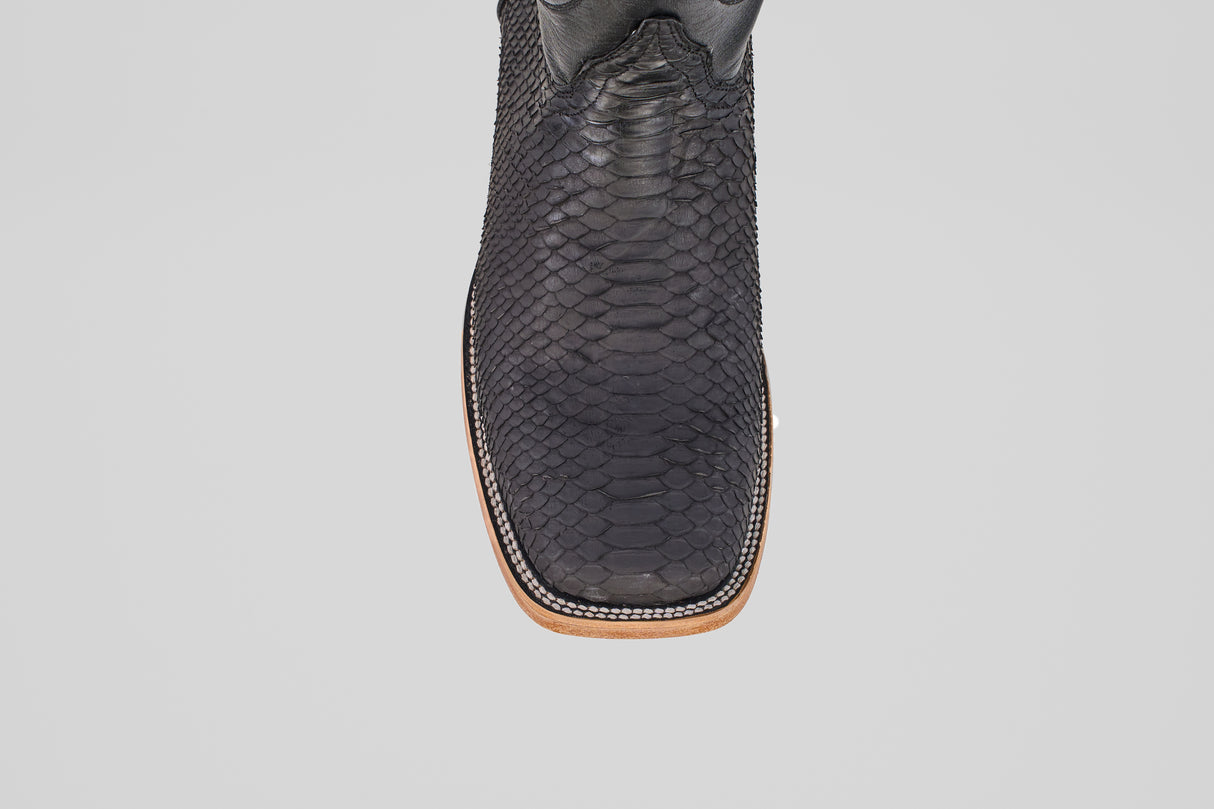 A close-up, top-down view of the Tanner - Matte Black - Square Toe cowboy boot with a light brown sole, set against a plain gray background.