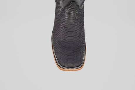 A close-up, top-down view of the Tanner - Matte Black - Square Toe cowboy boot with a light brown sole, set against a plain gray background.