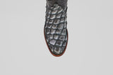 A close-up, top view of the Conor - Newspaper - Roper Toe boot showcases its textured, scale-like pattern and brown sole against a white background—a striking example of exotic leather craftsmanship.