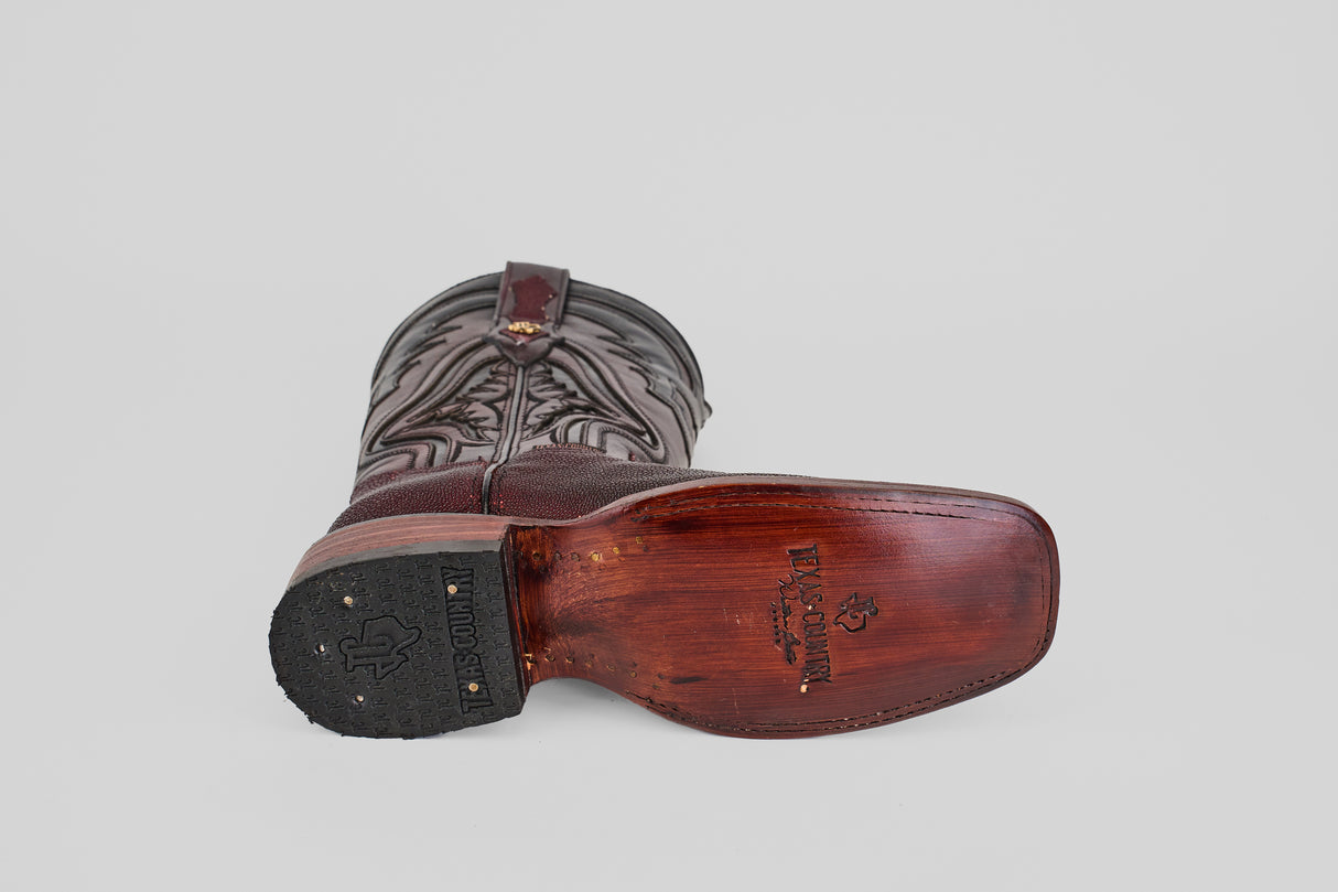 The Ranger – Wine – Rodeo Toe cowboy boot is shown on its side against a plain grey background, highlighting the worn brown leather sole and intricate stitching on the upper.