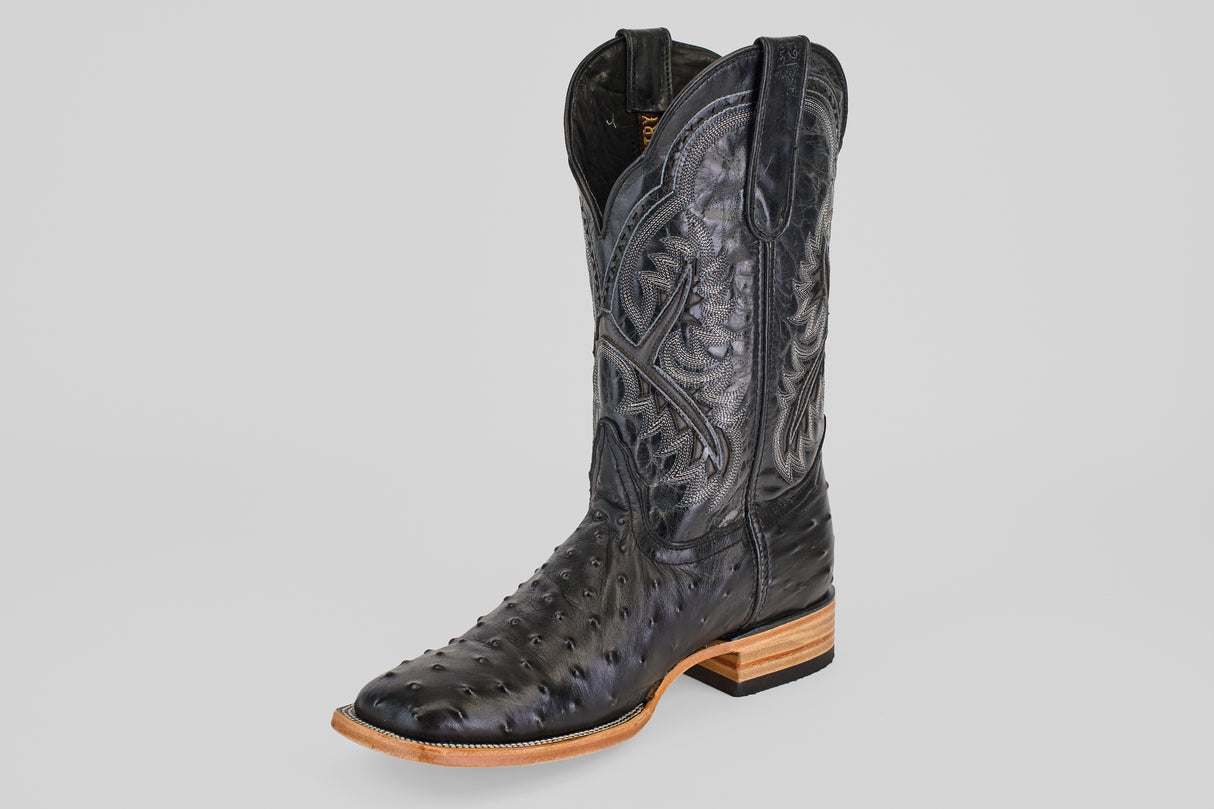 The Ostrich Black - Embossed Leather - Square Toe (E424) cowboy boot features decorative stitching, a high shaft, square toe, and tan stacked leather heel and sole. The textured black leather contrasts against a light gray background.