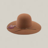 The 4X - Fawn - TC Hats is a wide-brimmed brown Western hat with a shapeable crown and thin string around the base, displayed on a light beige background. A purple hand-shaped tag is attached to the hat.