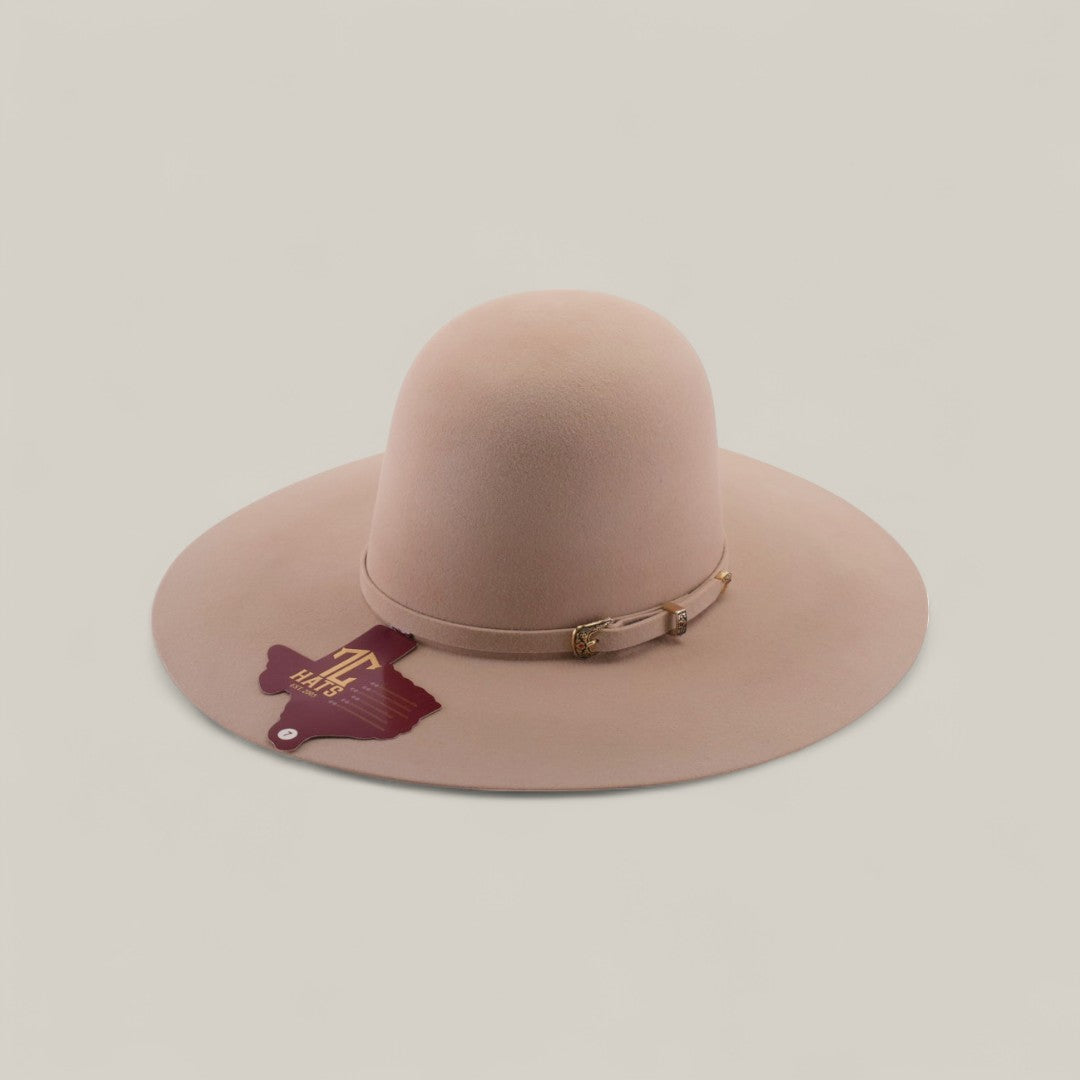 The 4X - Belly - TC Hats is a wide-brimmed, light pink felt Western hat with a thin matching band and gold buckle, maroon tag on the band, and a shapeable crown, shown against a plain light background.