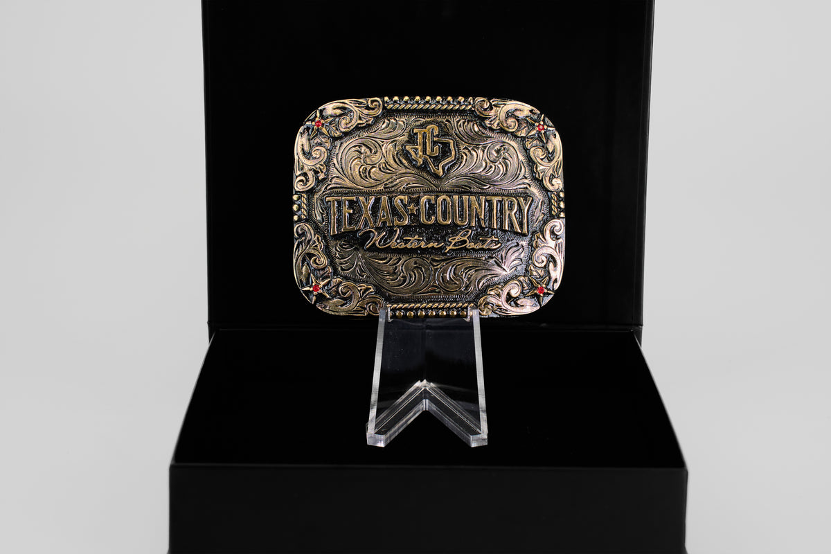 The Texas Country Buckle - Mod 4, a decorative gold and silver Western belt buckle engraved with Texas Country Western Belt, is displayed upright in an open black box—ideal for collectors.
