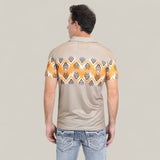 A man is seen from the back wearing the Mens Performance Fabric Aztec Panoramic Print Khaki Polo (PGP10607), featuring an orange and black Aztec design across the upper back and sleeves, paired with light blue jeans with stitched back pockets.