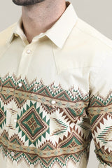 A man wears the Mens Western Modern Fit Cotton/Spandex Long Sleeve Beige Shirt with Snaps (WPL10677), featuring a pointed collar, geometric brown, green, and turquoise tribal pattern, pearl snap buttons, and long sleeves.