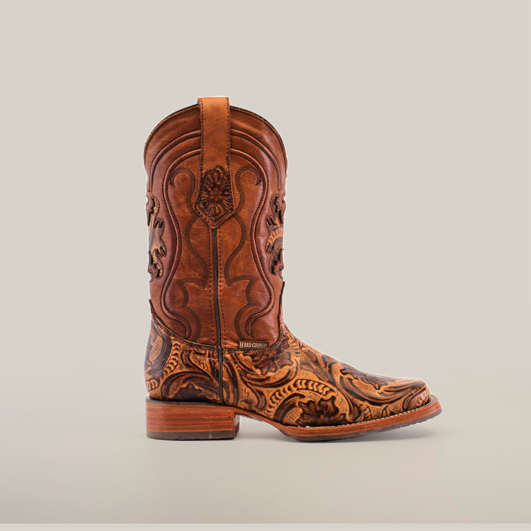The Handtooled Leave Orix boot, crafted from premium cowhide leather, features intricate embossed patterns and detailed stitching. With a low wooden heel and slip-resistant sole, it combines traditional Western style with practicality against a white background.