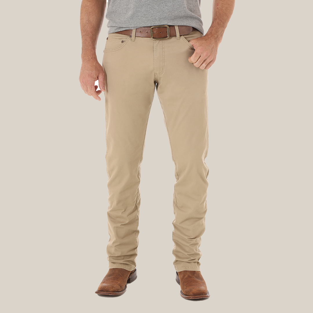 A person stands with their back to the camera, wearing a gray shirt and Mens Wrangler Retro Slim Fit Straight Leg Pant - 1088MWZFN in beige, noted for its visible pocket stitching and leather tag. Brown shoes complete the relaxed fit look.