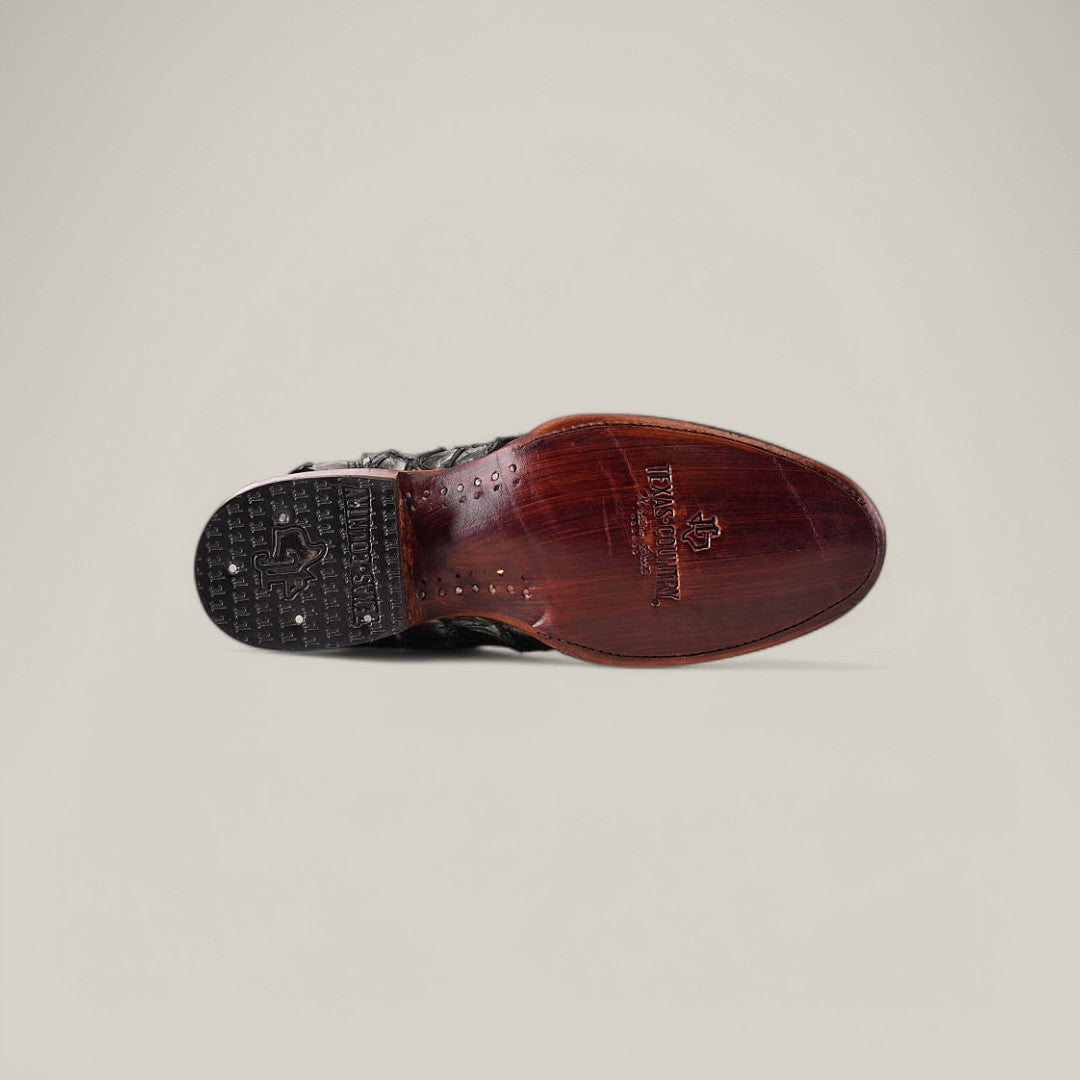 A single brown leather shoe, the Exotic Pirarucu Fish - Newspaper - Roper Toe, is shown from below with a textured black heel and smooth sole featuring a decorative logo. Crafted from luxurious materials, it exudes the elegance of luxury boots against a plain light gray background.