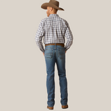 A modern cowboy stands with his back to the camera, wearing a plaid shirt, Ariat M7 Slim Ezra Straight Jeans - Brighton (10045388), brown boots, and a cowboy hat.