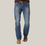 Wearing faded blue Mens Wrangler 20X No. 42 Vintage Bootcut Jean - 1042MWXLB, a person with a brown belt and leather shoes stands against a light background. The premium denim shows slight whiskering and offers a timeless, classic straight fit style.