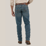 A person in Wrangler Mens 20X Extreme Relaxed Fit Jeans - 1044MWXMA, blue denim with a brown belt and shoes, stands against a white background. They sport an arm tattoo and light-colored rolled sleeves, epitomizing the relaxed style.