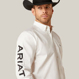 A man in a white ARIAT Team Logo Twill Classic Fit Shirt (10046825) glances left. His black cowboy hat pairs well with the subtle chest pocket logo and embroidered details, enhancing the timeless appeal of the shirts classic fit and plain white background.