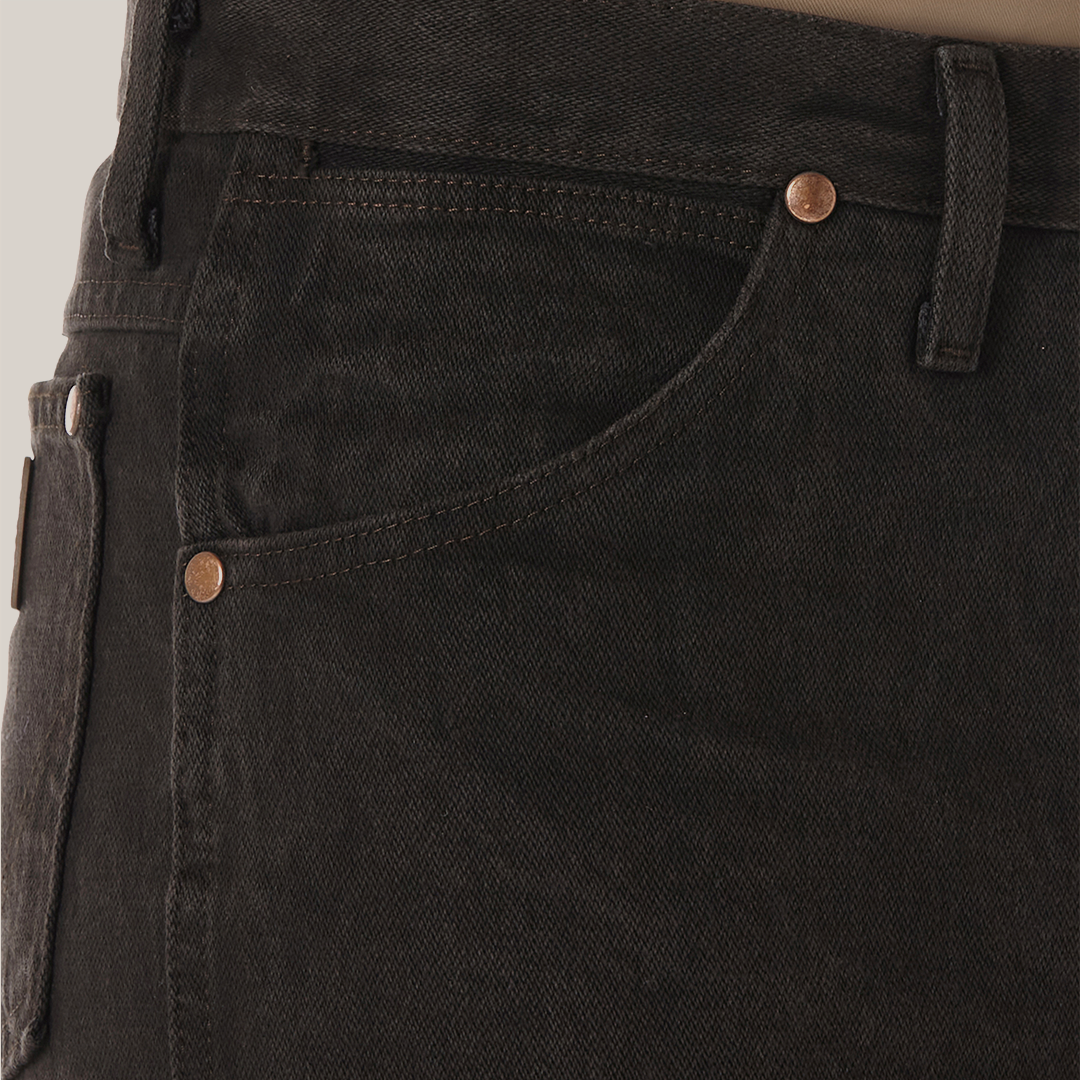 Close-up of someone wearing Wrangler Cowboy Cut Slim Fit Jean - 0936KCL in dark green with copper rivets, featuring a front pocket and belt loop. A brown shirt is neatly tucked in.
