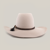 The 6X Brazil Belly is a beige wide-brimmed hat made from genuine sheep wool, featuring a tall crown and enhanced with a premium leather band with woven details and a small black feather.