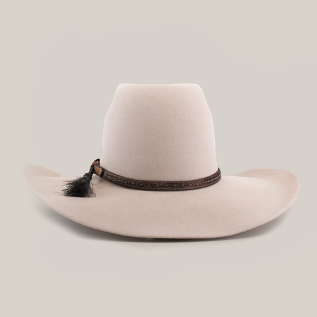 The 6X Brazil Belly is a beige wide-brimmed hat made from genuine sheep wool, featuring a tall crown and enhanced with a premium leather band with woven details and a small black feather.