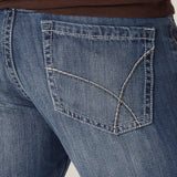 Close-up of a person in a plain, light-colored setting wearing brown shirt and Mens Wrangler 20X No. 42 Vintage Bootcut Jean - 1042MWXLB, featuring detailed back pocket stitching.