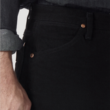 A person in a dark denim shirt with rolled sleeves and wearing Wrangler Cowboy Cut Slim Fit Jean - 0936WBK. The photo highlights the premium denims pocket, showing stitching and copper rivets, as their hand rests relaxed by their side.