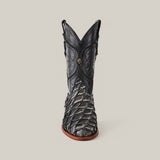 The Exotic Pirarucu Fish - Newspaper - Roper Toe is a luxurious black cowboy boot made from textured Pirarucu leather, showcasing intricate stitching and a front emblem, elegantly standing against a plain gray background.