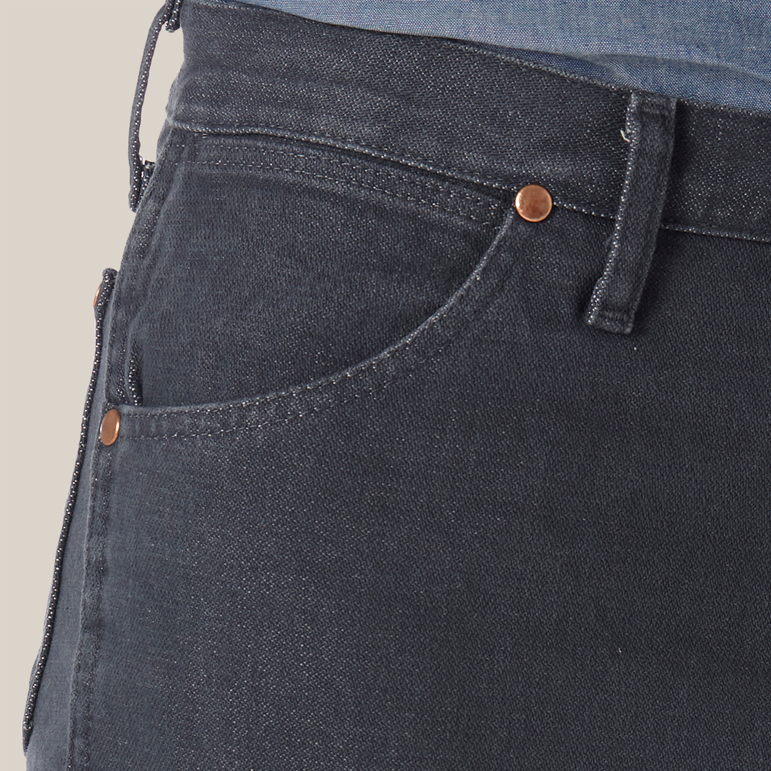 Close-up of someone in Wrangler Cowboy Cut Slim Fit Jeans - 0936CHG, featuring dark denim, visible stitching, and copper rivets on the pocket; paired with a tucked-in blue denim shirt to highlight premium denim quality.