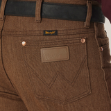 Close-up of a person wearing Wrangler Cowboy Cut Slim Fit Jeans - 100936BKW with a black belt. The jeans feature a branded leather patch above the right pocket and a small tag on the waistband, paired with a dark red shirt for classic style and rugged elegance.