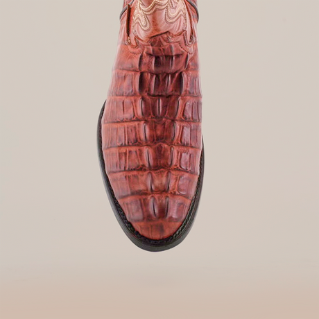 The Crocodile Tail Print Cogñac boot features a brown crocodile tail print on the front, intricate upper stitching for a decorative flair, and a premium dark leather sole that contrasts with the lighter upper. The plain light background highlights the boots unique details.